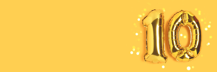 Banner with number 10 golden balloons with place for text. Ten years anniversary celebration concept on a yellow background with glowing bokeh.