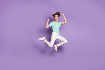 Fototapeta na wymiar Full size profile photo of nice optimistic girl jumping wear white sneakers pants blue t-shirt isolated on violet color background