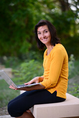 portrait of beautiful and cheerful mature woman working outdoor in a park with wireless connection and a laptop computer