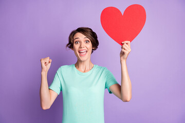 Photo of lucky young woman dressed casual turquoise clothes holding pointing big red heart arm fist isolated violet color background