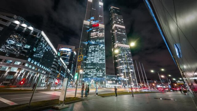 Beautiful motion timelapse of big city busy street in the night. Modern skyscrapers glitter with neon lights, heavy traffic passing by and pedestrians crossing the intersection in the center of Moscow
