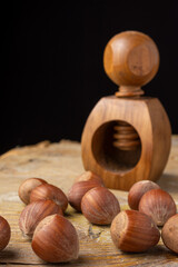 Top view of hazelnuts and wooden nutcracker on rustic wooden table, black background, vertical