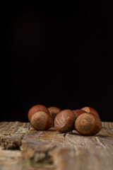 Close-up of hazelnuts on rustic wooden table, with selective focus, black background, vertical, with copy space