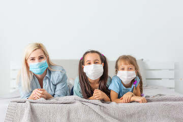 Family in medical face masks lying on a bed quarantine during a COVID-19 coronavirus epidemic