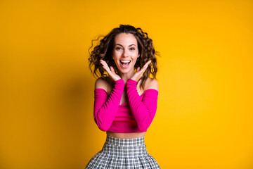 Photo portrait of excited woman holding hands near face smiling wearing pink crop-top checkered skirt isolated on vivid yellow colored background