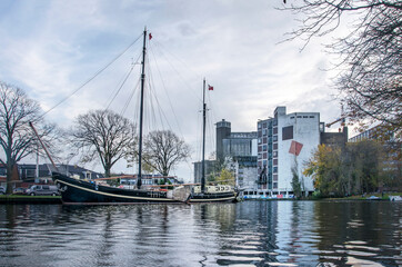 Fototapeta na wymiar Leiden, The Netherlands, November 14, 2020: view of the city's ramparts canal with a historic sailboat and the monumental flour factory