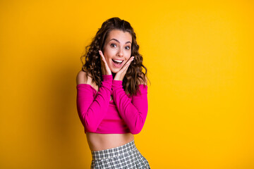 Photo portrait excited woman reacts to hearing about big sales discounts holding hands to face open mouth wearing pink top checkered skirt isolated on vivid yellow colored background