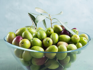 Freshly picked raw green olives in glass bowl on textured background.
