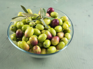 Freshly picked raw green olives in glass bowl on textured background.