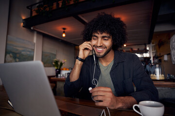 Handsome young man with curly hair watching videos on laptop with earphones in cafe