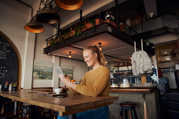 Beautiful smiling business woman sitting in cafe using digital tablet and drinking coffee