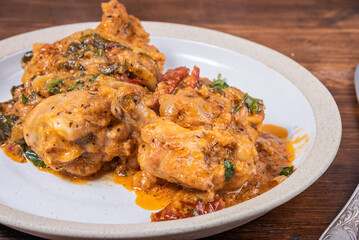 Ready Italian dish - Tuscan chicken with sun-dried tomatoes, tomato paste, spinach, cream and cheese on a plate on a wooden table