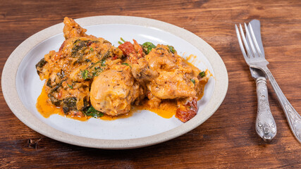 Ready Italian dish - Tuscan chicken with sun-dried tomatoes, tomato paste, spinach, cream and cheese on a plate on a wooden table