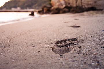 Footprints in the sand of the beach, in the background a stone coast in the sunrise