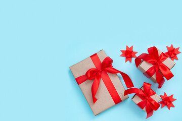 Three gift boxes with a red bow and origami paper stars on a pastel blue background. Minimal festive composition. Copy space for text.
