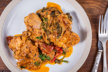 Ready Italian dish - Tuscan chicken with dried tomato and cream sauce with cheese and onions on a plate on a wooden table, top view, close-up