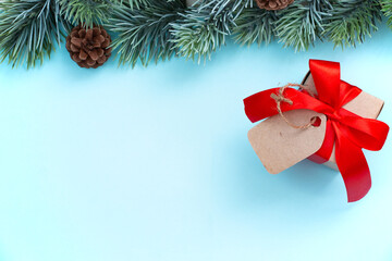 Fir branch, a gift with a red bow and a tag for text on a pastel blue background. Minimal festive composition. Copy space for text.