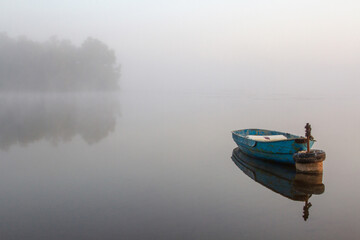 Foggy dawn over the lake. Lonely boat on the water.