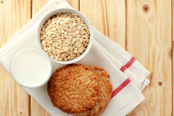 Oat cookies with oat flakes and cup of milk on wooden table