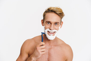 Joyful caucasian shirtless man shaving with foam and razor