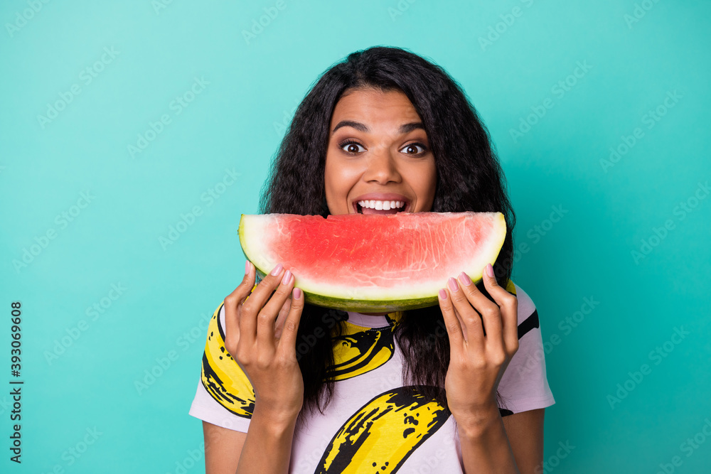 Wall mural photo of excited dark skin girl bite natural watermelon slice wear pink t-shirt isolated on turquois