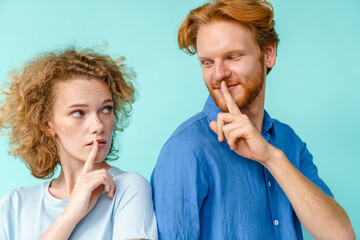 Young pleased redhead couple showing silence gesture