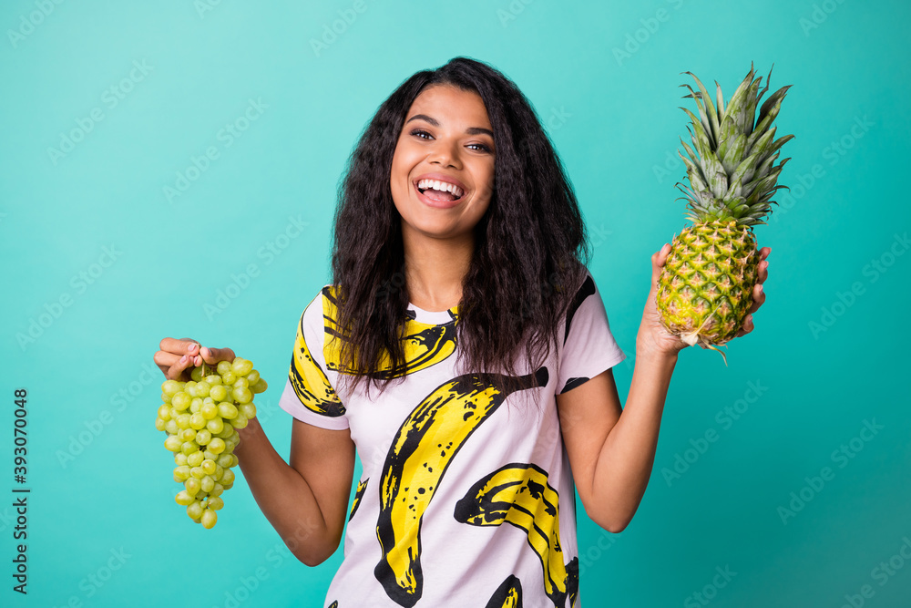 Wall mural Photo of positive dark skin girl enjoy hold pineapple grapevine isolated over turquoise color background