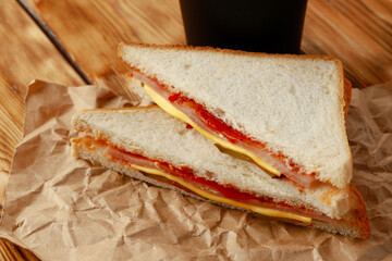 Toasted sandwich in craft paper with cup of coffee on table