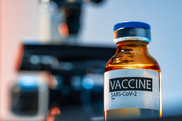 Vial of Covid-19 vaccine next to a microscope