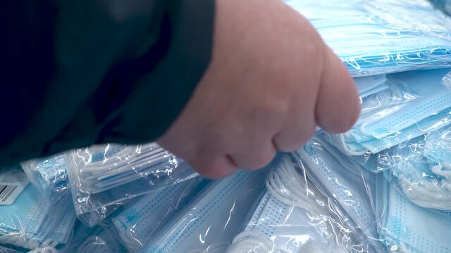A woman's hand takes a package of medical masks. Many new medical masks in packages. New unopened packages of medical masks, close-up