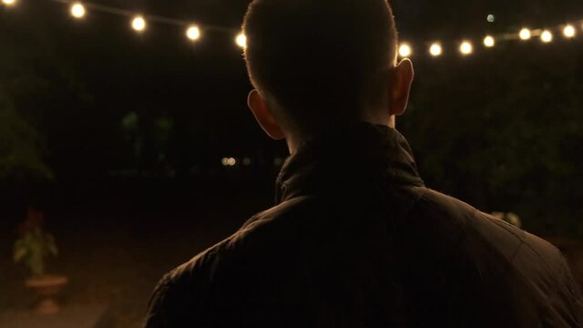 Young short-haired man walks through the night fair under the lights and looks over his shoulder