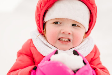 Happy child girl portrait walking and playing with snow in winter park, the concept of a holiday. Emotions of happiness. Winter vacation in the mountains.