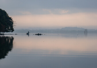 朝靄漂う海　小舟の上で網を引く男性