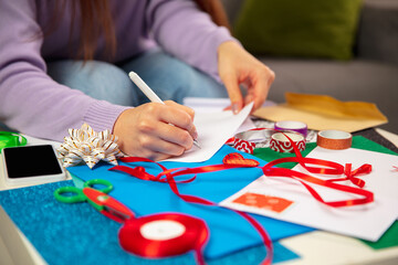 Close up female hands making greeting card for New Year and Christmas 2021 for friends or family,...