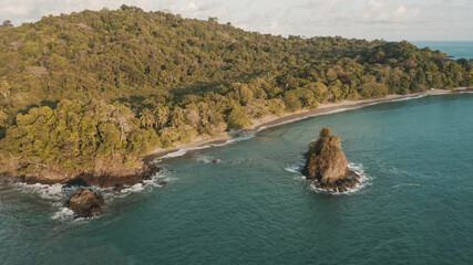 A beautiful wavy sea with immense rock formations and coastline covered with lush vegetation