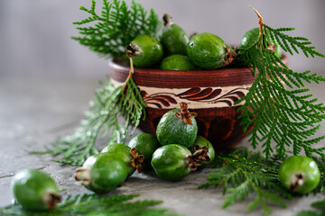feijoa fruits in a brown clay plate with scattered feijoa fruits on a gray background with thuja leaves macro photo
