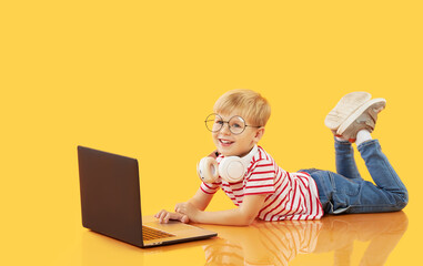 Litttle child boy using laptop on yellow background. Education, online study, home studying, distance learning. Primary school student during quarantine