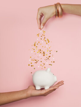 Black woman hands putting in money box golden confetti stars on pastel pink background