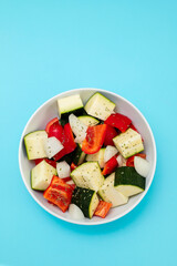fresh vegetables in cubes in the white bowl on blue background