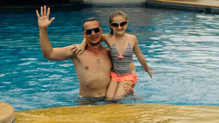 The father with little daughter have fun in the pool. Dad plays with the child. The family enjoy summer vacation in a swimming pool. Slow motion.