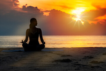 Meditation and zen for healthy concept. Silhouette young woman practicing yoga while sitting on the beach with beautiful sunrise in the morning.