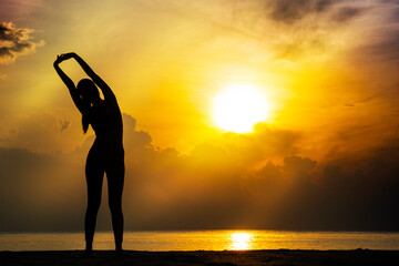 Lifestyle relax exercise concept. Silhouette young woman stretching her slim body before workout while standing on the beach with beautiful sunrise in the morning.