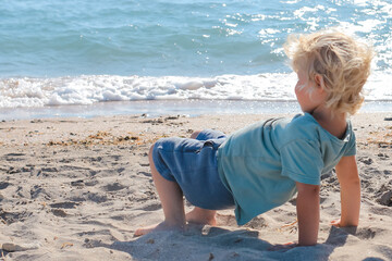 Little boy walking and playing alone on the beach. Summertime, vacation, travel, nature concept.