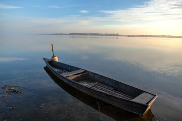 Naklejka na ściany i meble Foggy dawn over the lake. A lone boat on the water.