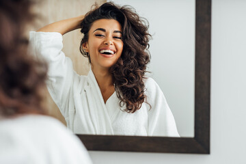 Happy woman in bathroom. Young female playing with her hair in front of a mirror. - obrazy, fototapety, plakaty