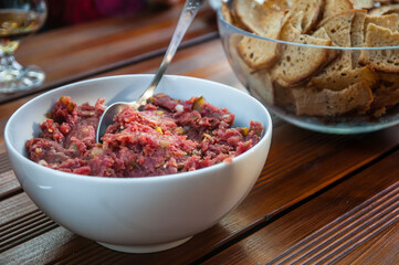 Homemade steak tartare in a bowl with bread chips served on wooden table