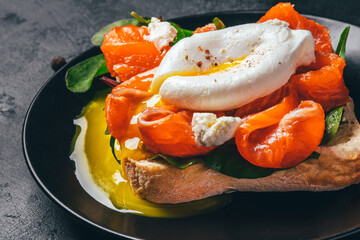 Sandwich with salmon, cheese, herbs and poached egg on black background.