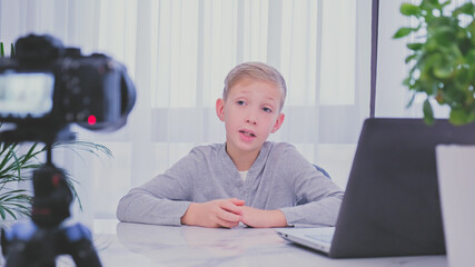 Child blogger videotapes his vlog at home. Boy recording his video blog. White boy speaks in front of a video camera for his blog channel. Little 8 year vlogger makes online streaming using smartphone