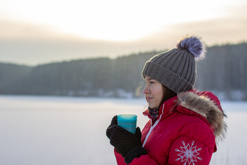 Fototapeta na wymiar Beautiful girl in a winter jacket with a mug in winter in nature.