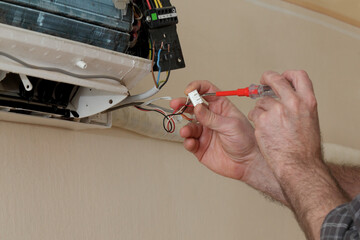 Electrician servicing air condition device in a room using screwdriver